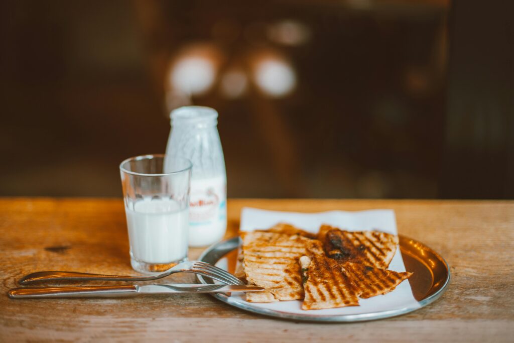 Glass of milk next to a sandwich on a table illustrating lactose intolerance vs dairy sensitivity and milk allergy.