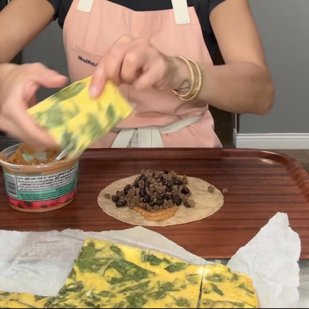 Assembling high protein breakfast burritos with sheet pan eggs, black beans, lean ground beef, cheese, and chipotle sauce