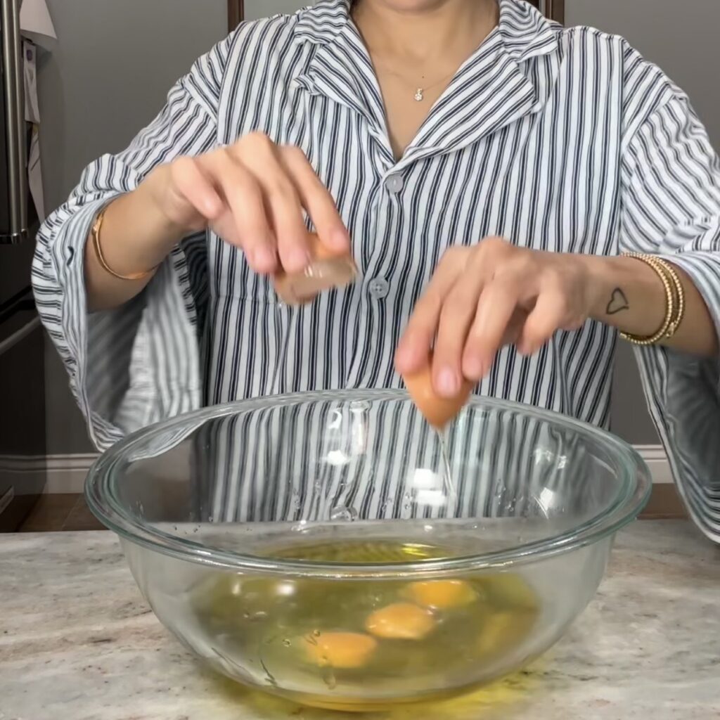 Cracking eggs into a mixing bowl to make lemon olive oil cake