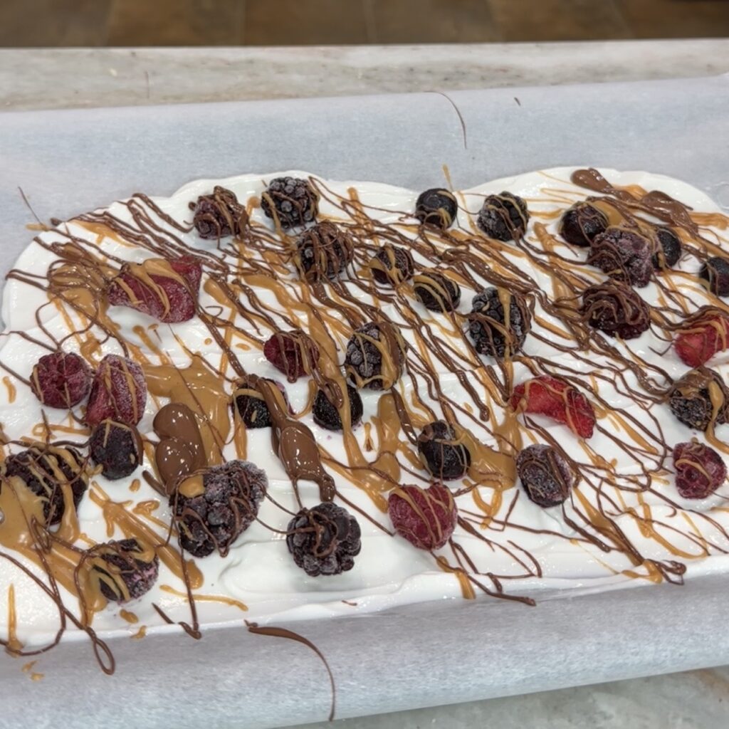 Frozen Greek yogurt berry bark topped with mixed berries, peanut butter, and chocolate.