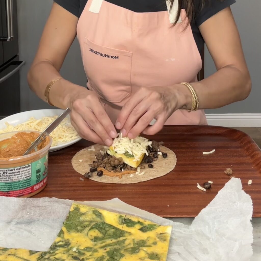 Assembling high protein breakfast burritos with sheet pan eggs, beef, cheese, and chipotle sauce.