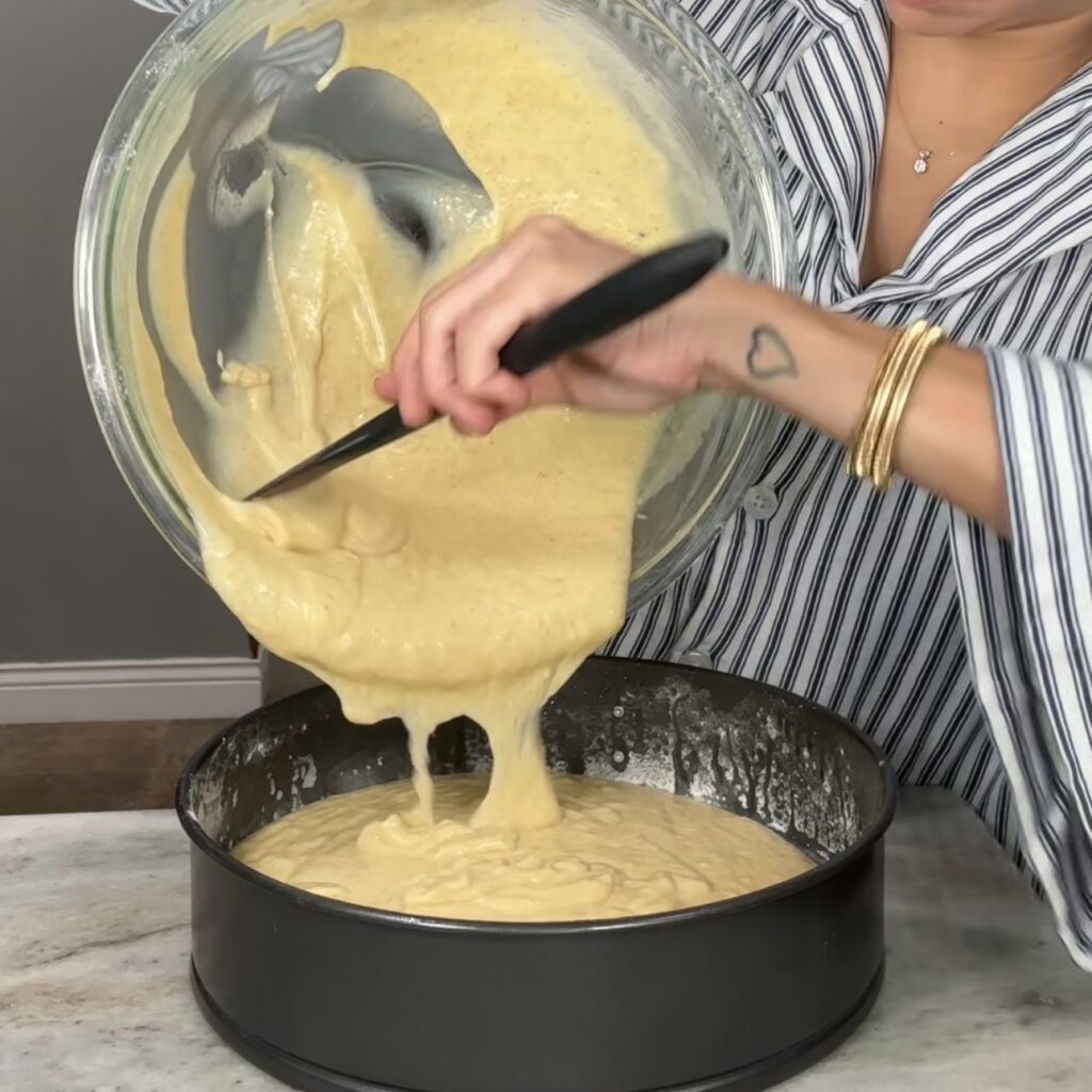Pouring lemon olive oil cake batter into a prepared cake pan before baking
