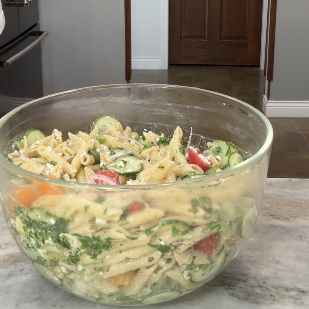 Mediterranean chickpea pasta salad with protein pasta, feta cheese, cucumber, tomatoes, olives, and parsley.